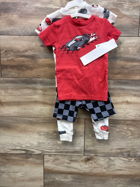 Front view of toddler 4-piece race car pajama set: red tee with car graphic, checkered shorts, white car-print pants on floor