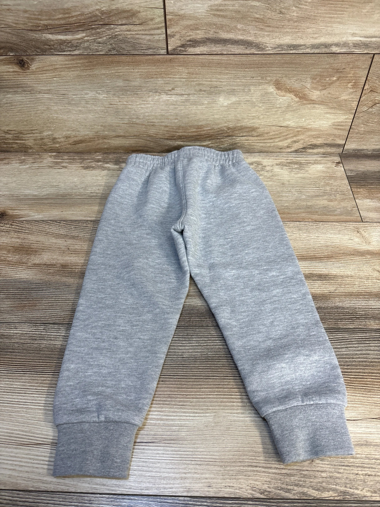 Gray kids sweatpants with elastic waist and cuffs, laid flat on wood floor