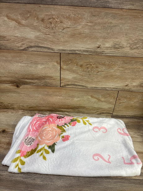 Folded view of white milestone blanket showcasing floral print and pink numbers with a wood plank background