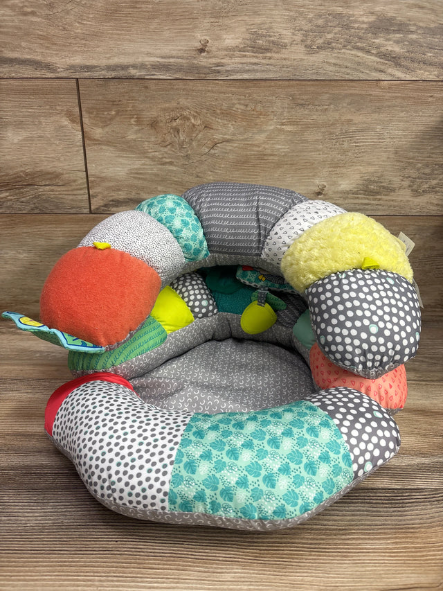 Top view of Infantino 2-in-1 Tummy Time and Seated Support showcasing colorful patterned cushions and attached toys on a wood floor