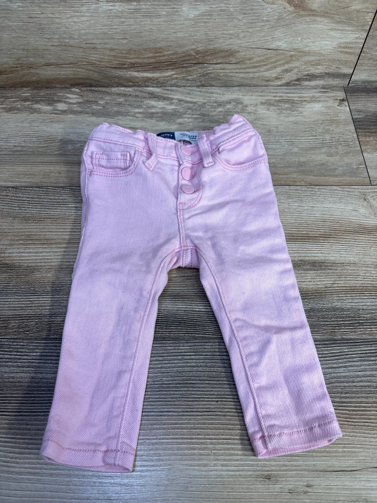 Front view of pink Old Navy toddler rockstar jeggings showing three-button fly and faux front pockets on light wood background