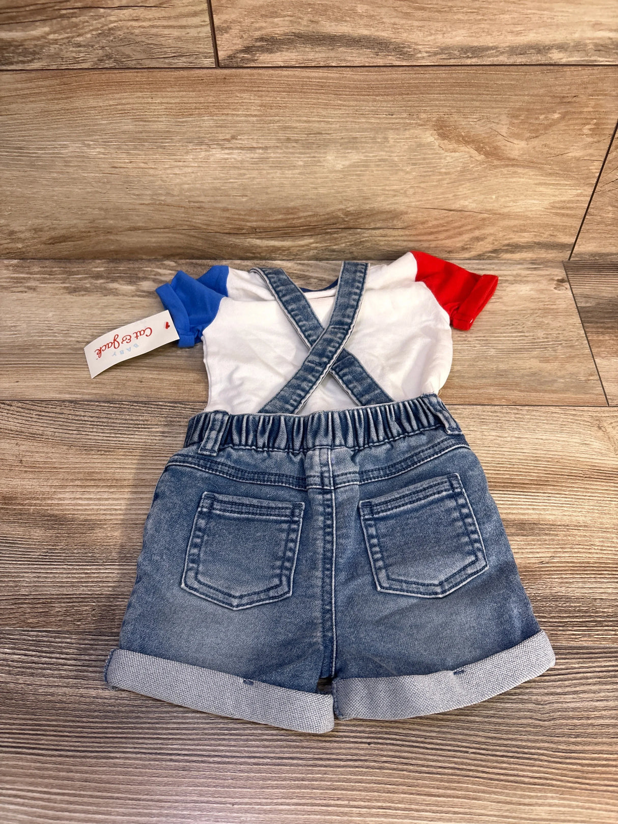 Flat lay of Cat & Jack denim suspender shorts set showing crossed suspenders, elastic waist and rolled cuffs on wood floor