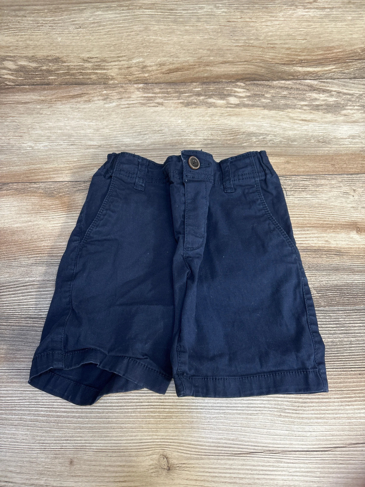 Navy blue toddler shorts with button waist, laid flat on wood floor for kids clothing resale