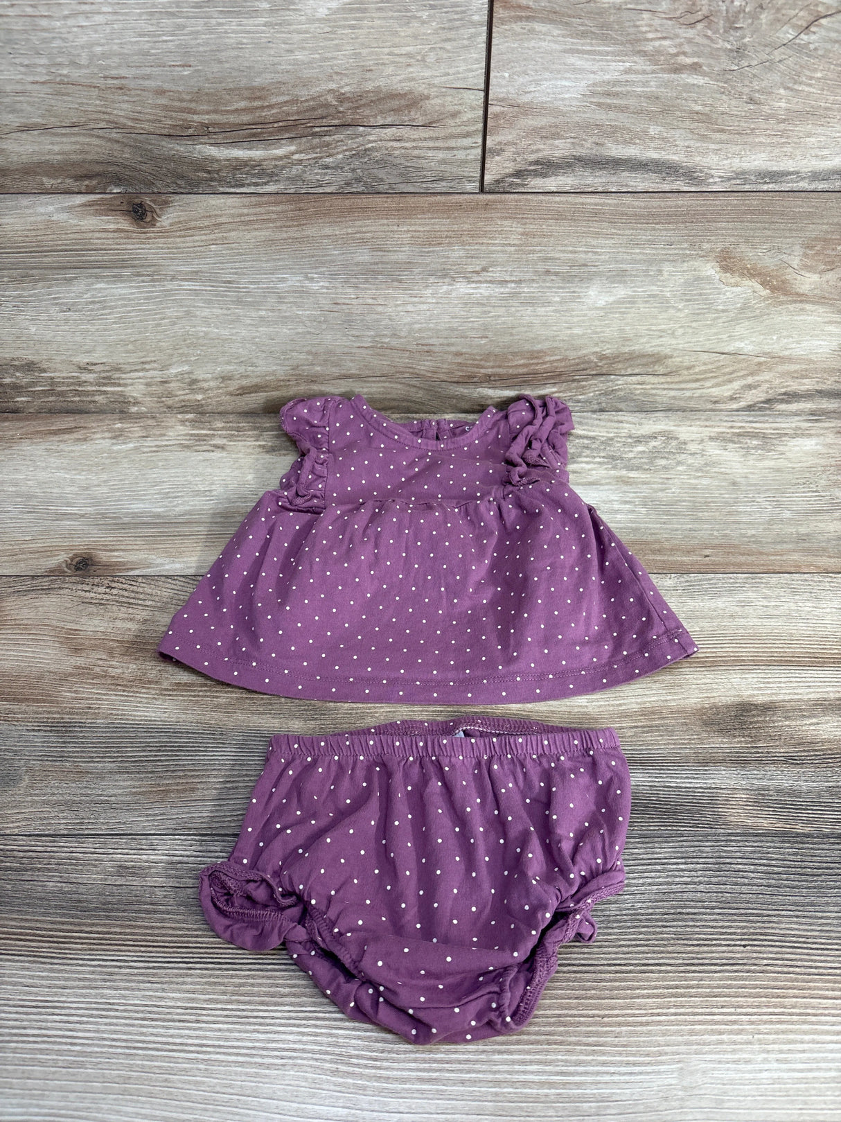 Purple baby outfit with white polka dots, including a ruffled sleeveless top and matching bloomers on wood floor