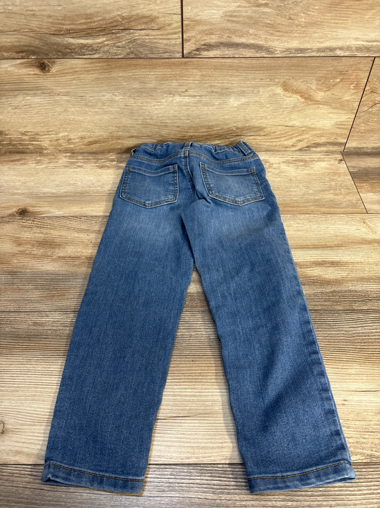 Kids' blue denim jeans with elastic waist, laid flat on wood floor