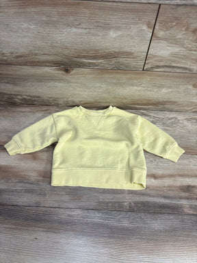 Front flat lay of Zara yellow baby sweatshirt size 6-9 months showcasing crewneck and ribbed cuffs and hem on wood background