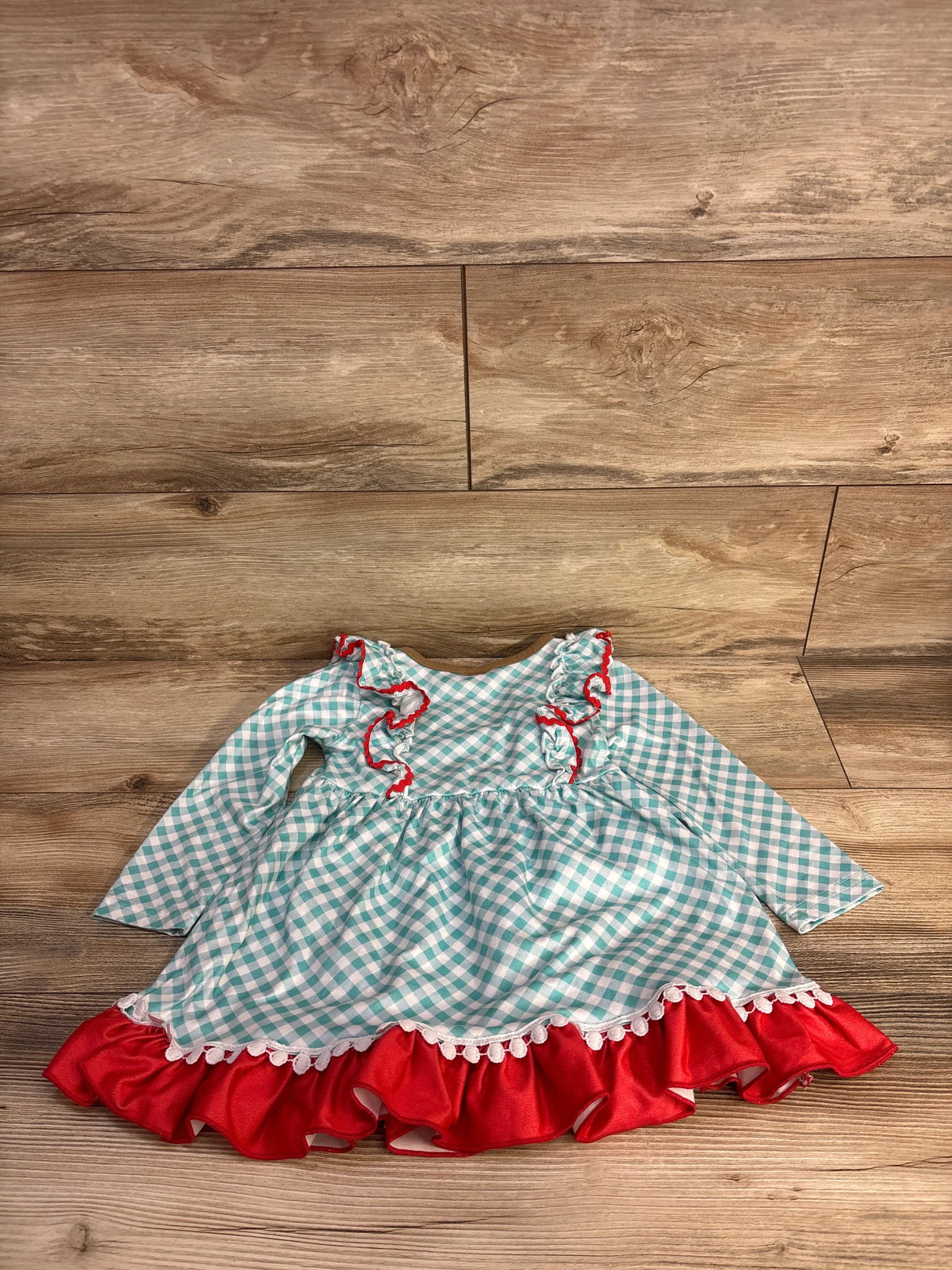 Flat lay of toddler cowgirl dress in blue gingham with red ruffled hem and chest trim on wood floor
