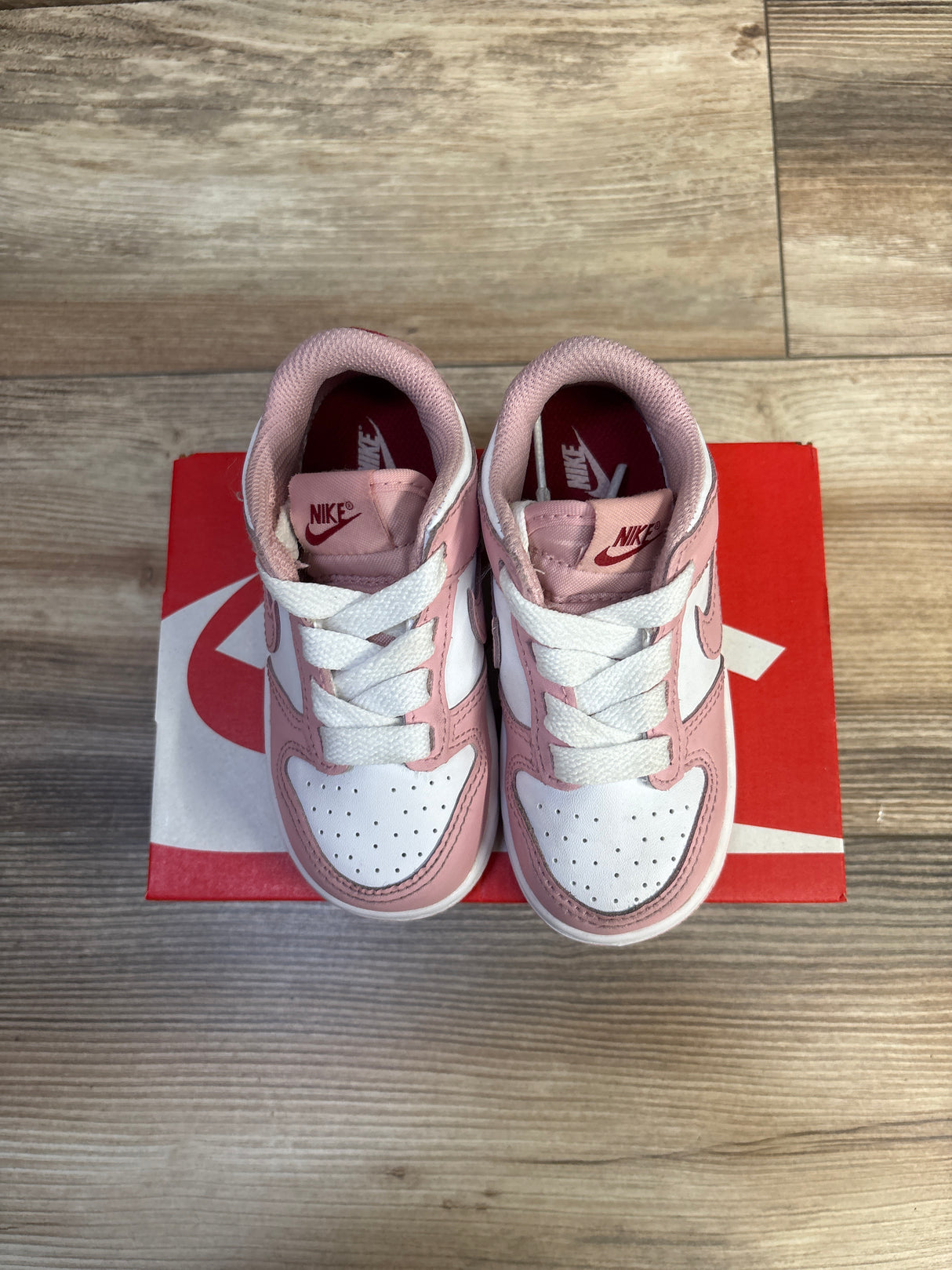 Top-down view of toddler Nike Dunk Low sneakers in pink glaze and white showing perforated toe, white laces, and Nike logo on red box