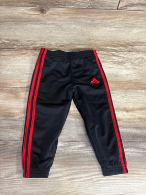 Black Adidas toddler track pants with red stripes and logo on wooden floor