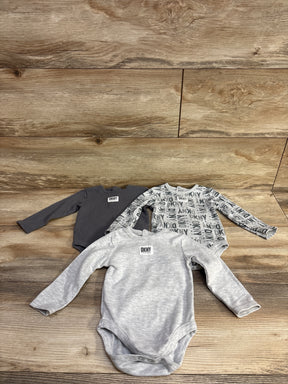 Three long-sleeve DKNY baby bodysuits in gray, black, and gray with logo print, displayed on wooden surface