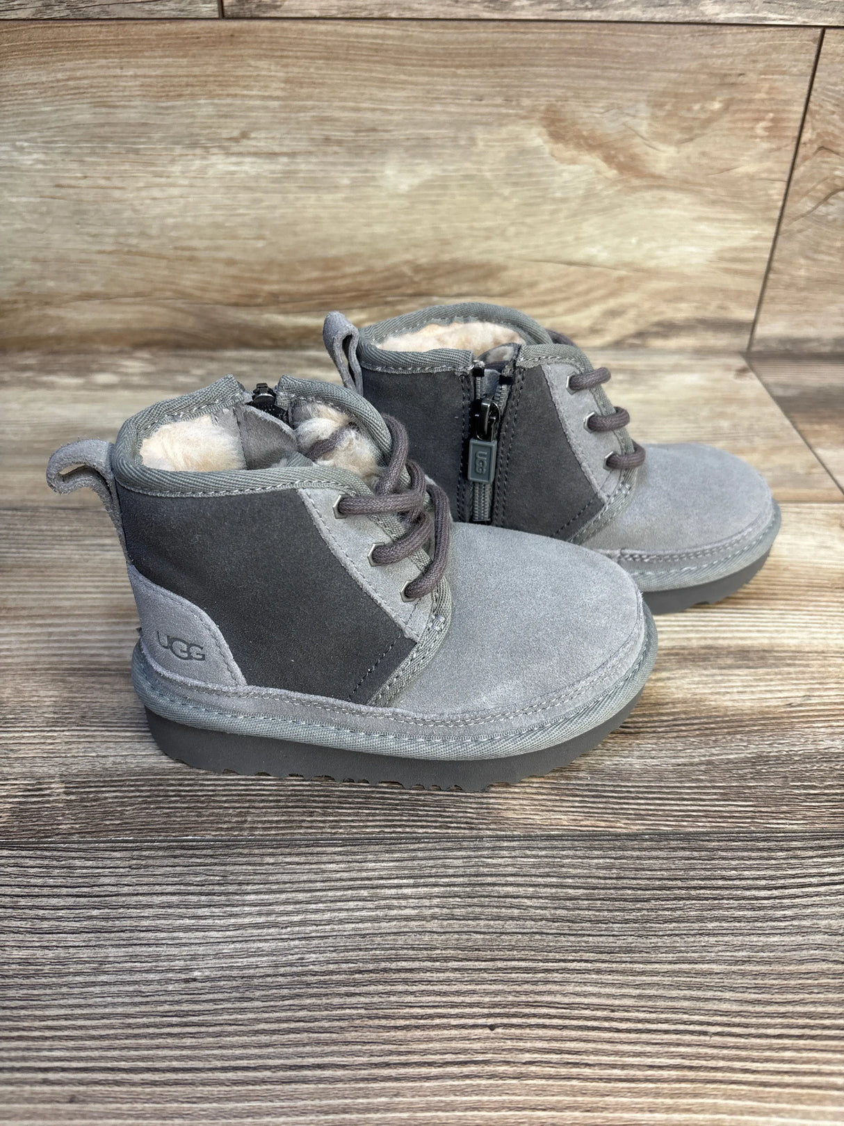 Three-quarter view of Ugg Neumel II boots in grey suede with shearling lining, side zipper and laces on wood background