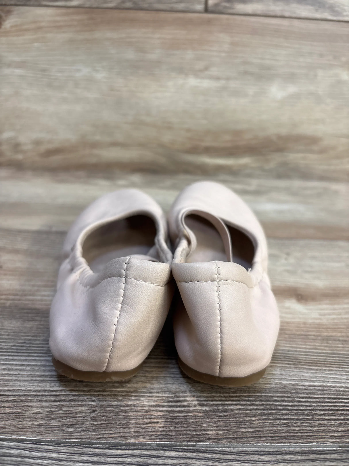 Light pink toddler ballet flats on wood floor, gently used children's shoes resale