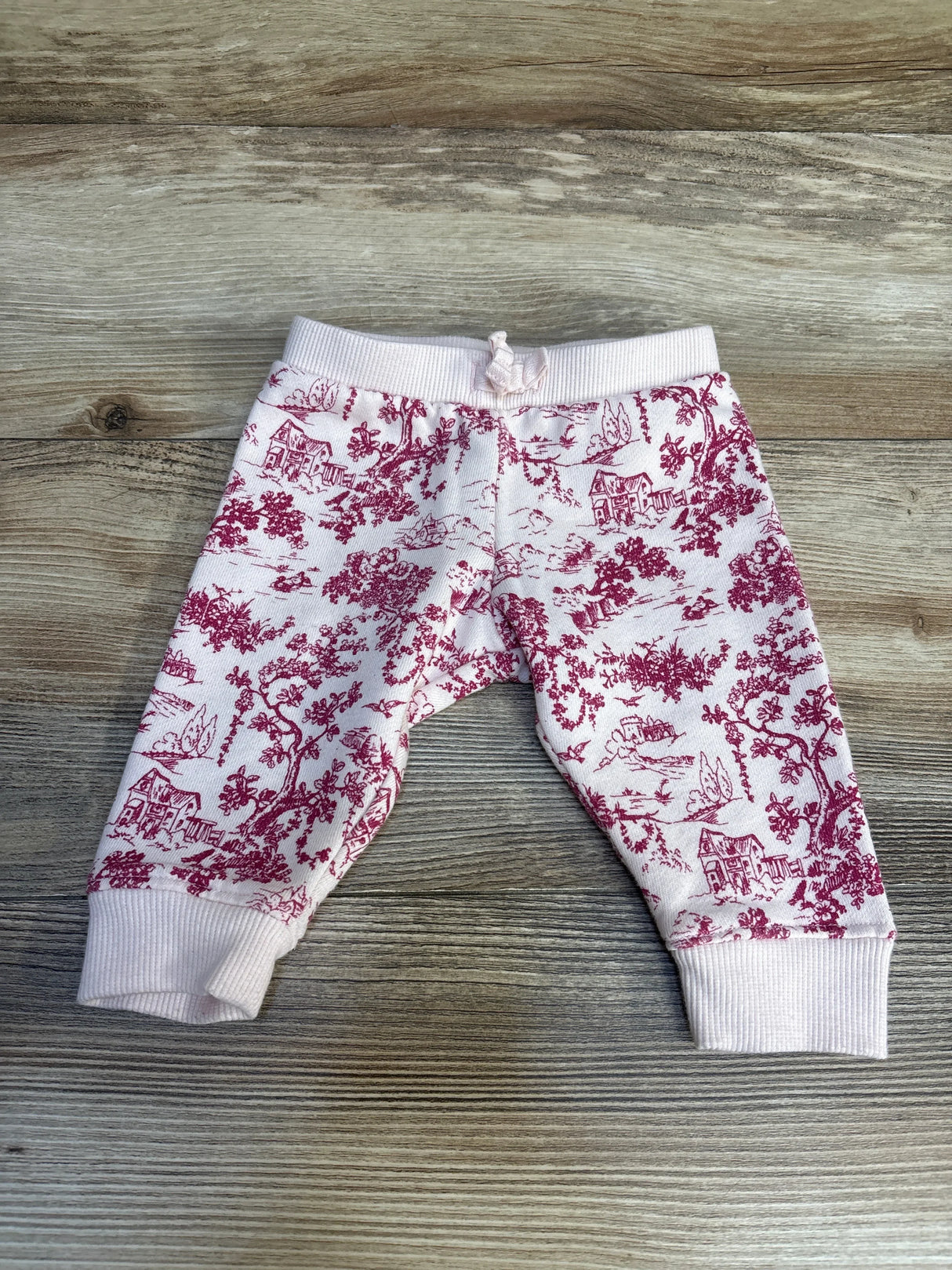 Pink baby pants with maroon countryside print on wood surface