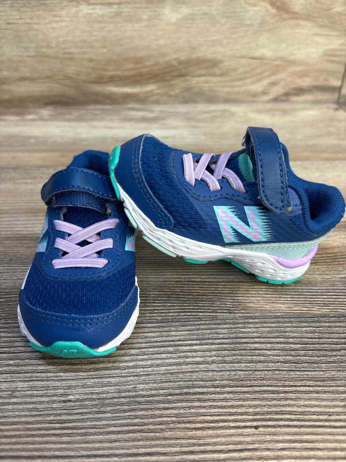 Navy blue toddler sneakers with velcro straps and purple laces on wood background