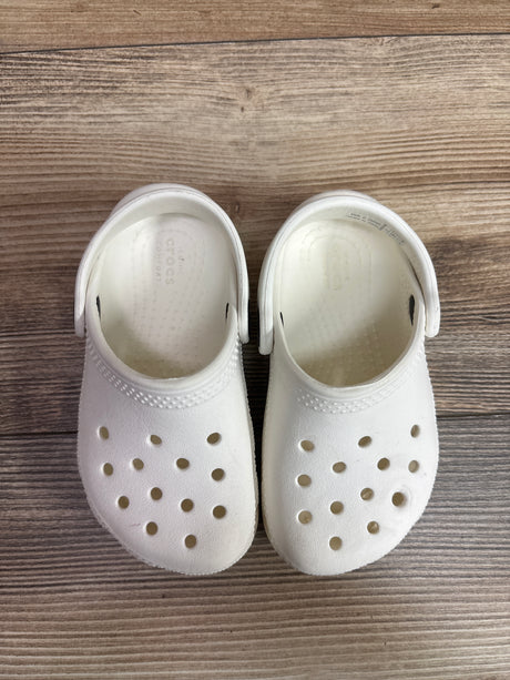 Top view of white Crocs Classic Clogs in child size 7C showcasing perforated uppers and heel straps on a wood grain background