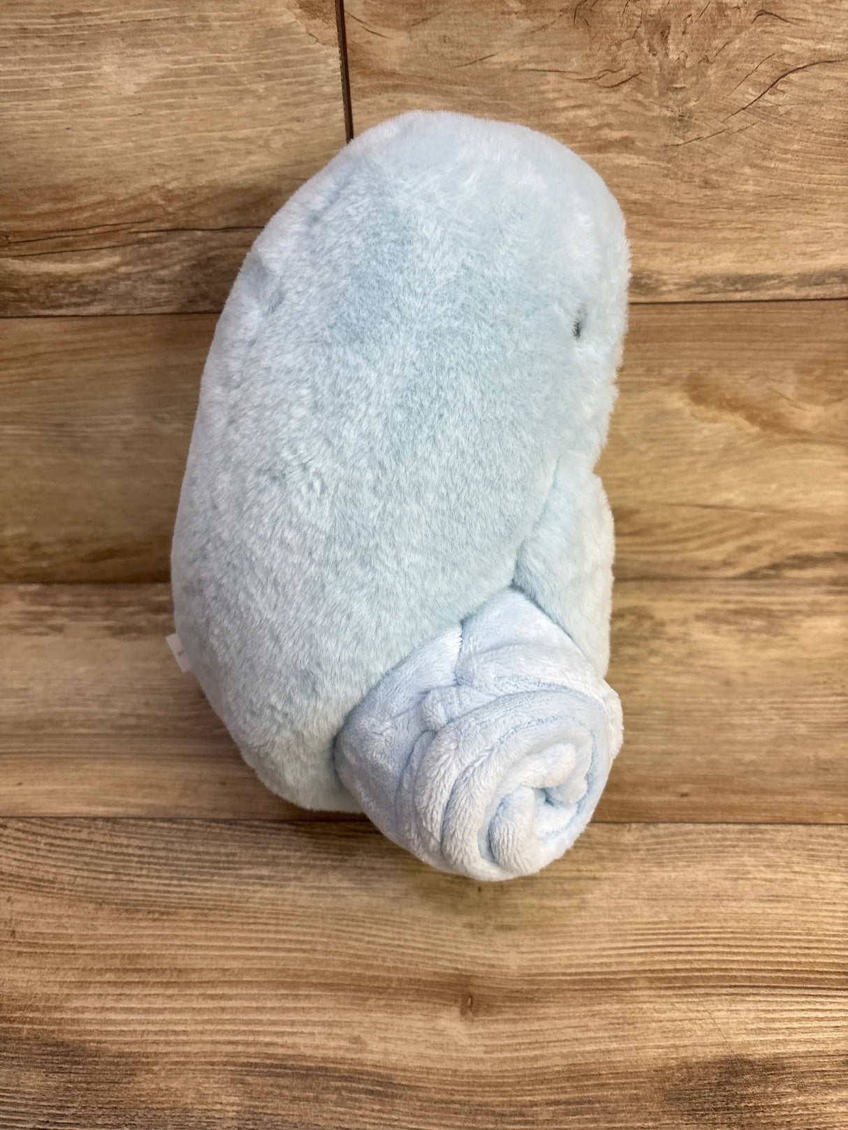 Three-quarter rear view of Cloud Island plush blanket with blue whale toy showcasing attached rolled blanket on wooden floor background
