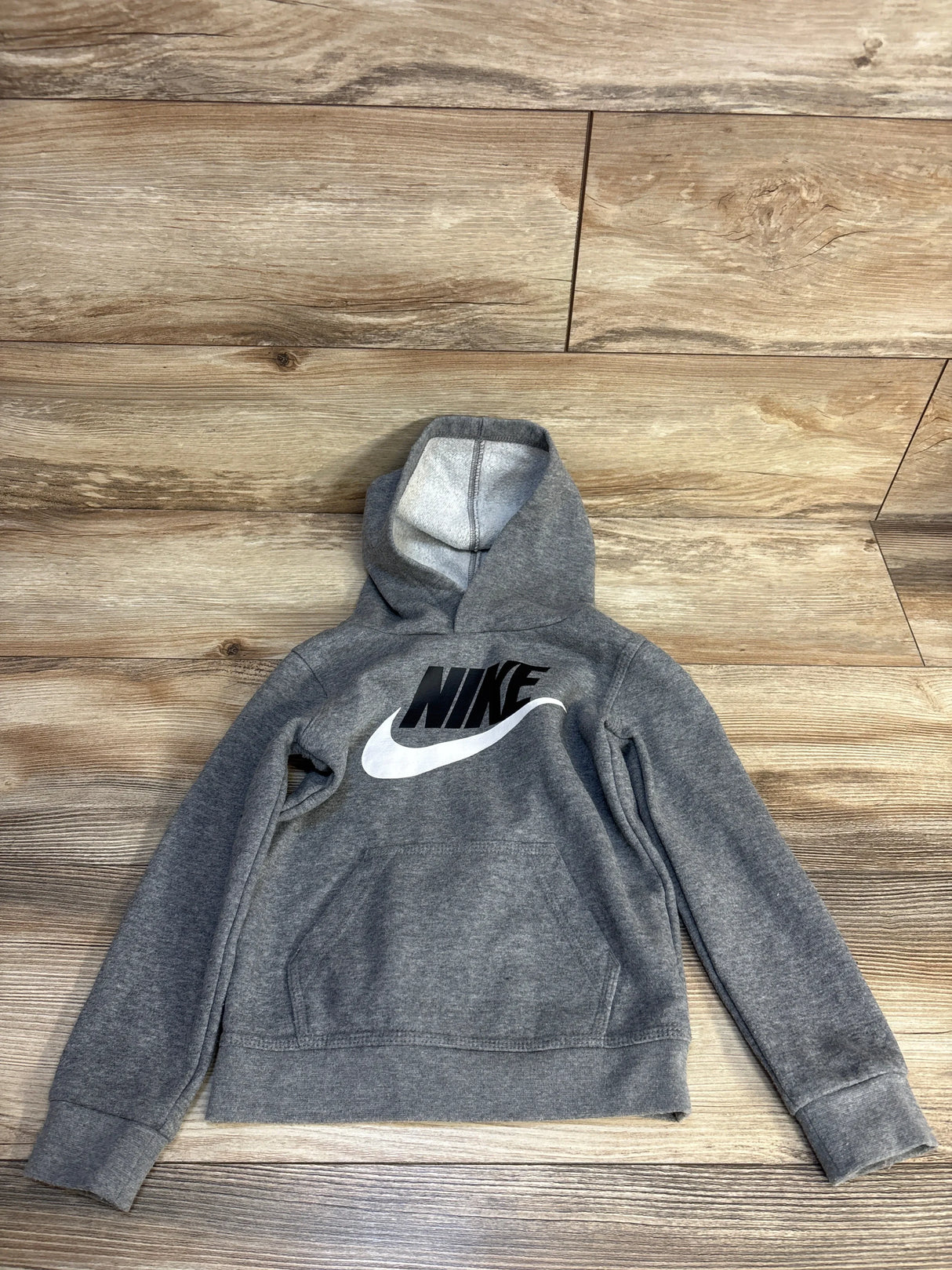 Gray Nike kids hoodie with black logo, laid flat on wood floor for resale