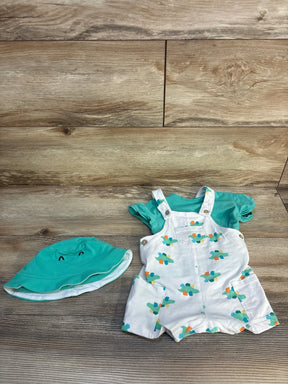 Front view of 3-piece turquoise dinosaur dungaree set: white romper with teal/orange dinosaur print, teal tee and hat on wood