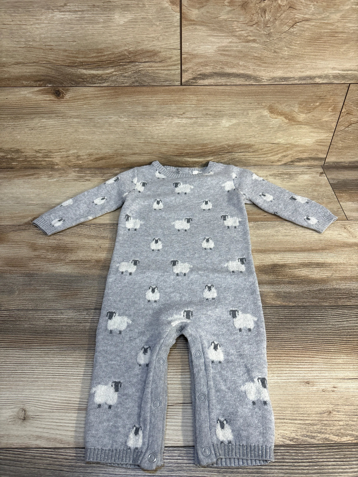 Gray knit baby romper with sheep pattern and snap buttons, laid flat on wood floor