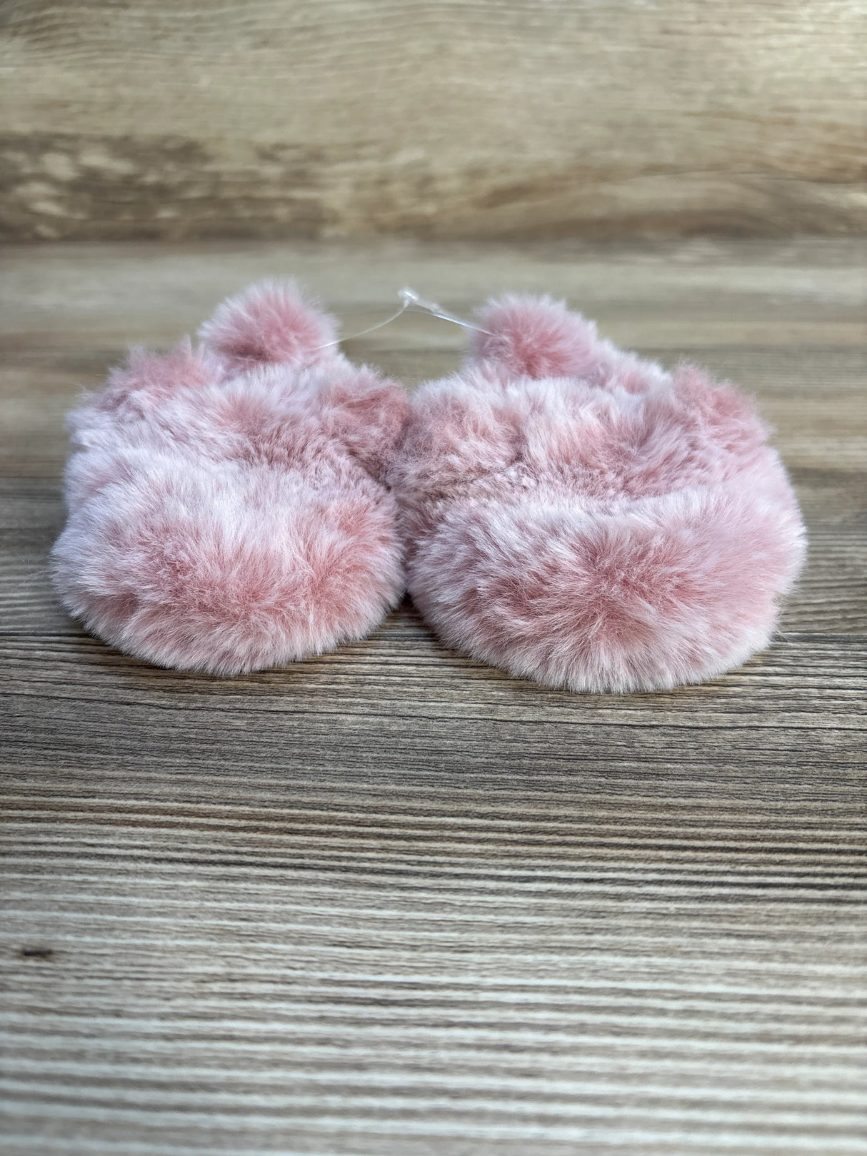 Pink fuzzy baby slippers with pom poms on wooden background