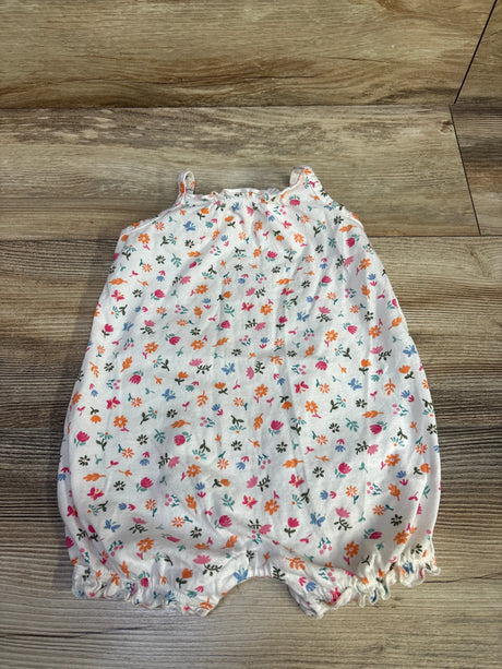 Flat lay of Carter's white shortie romper with multicolor floral print, thin straps, and elastic ruffled legs on wood