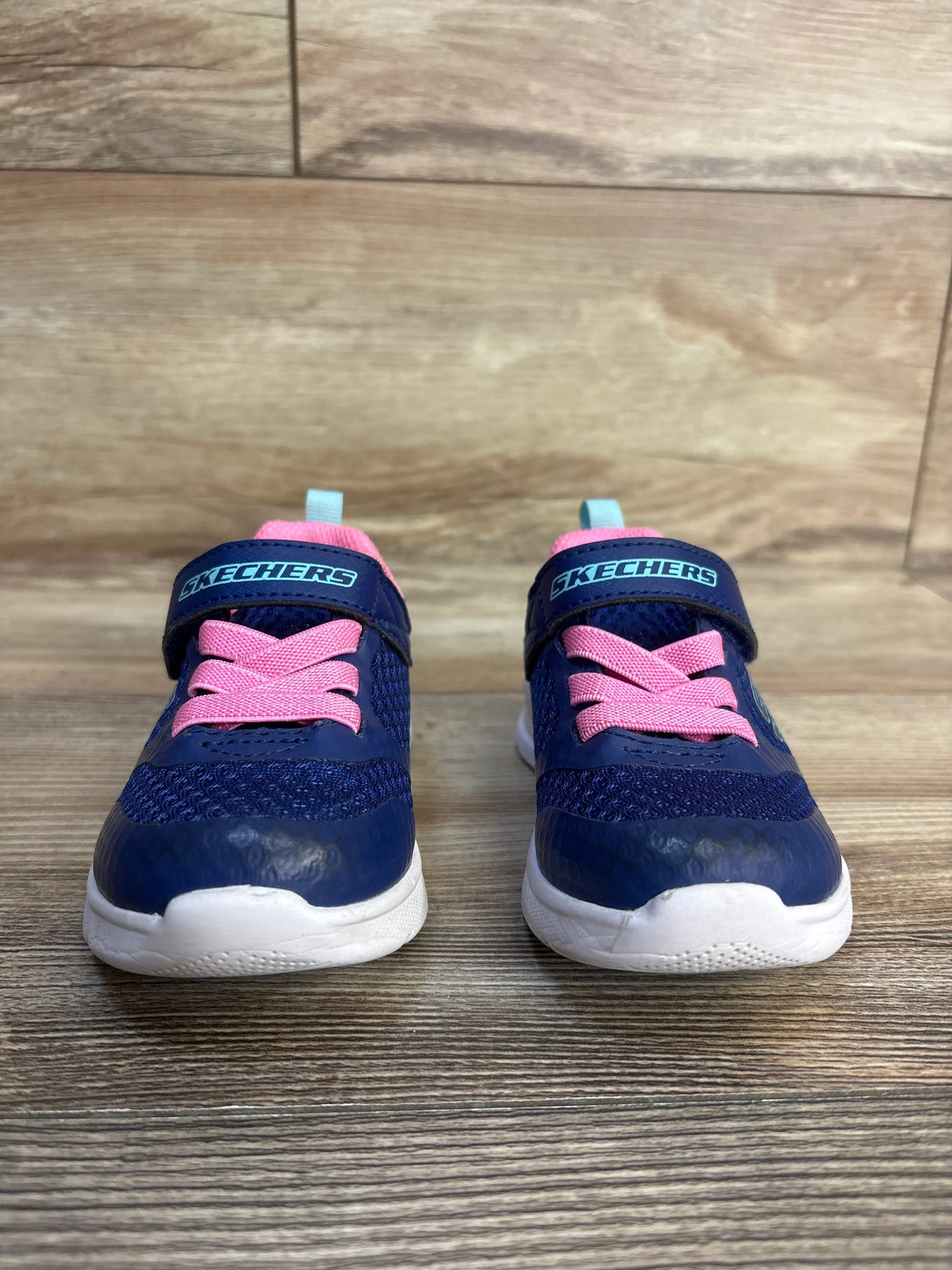 Navy blue Skechers toddler sneakers with pink laces and white soles on wood floor