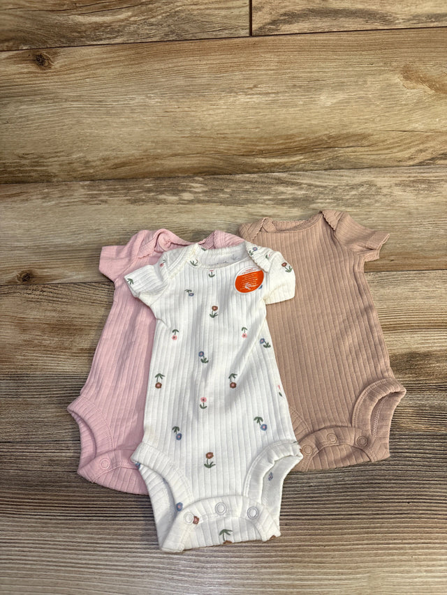 Flat lay of three preemie ribbed bodysuits, white floral, pale pink, and mauve, showing short sleeves and snap crotch on wood background