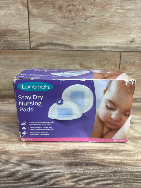 Front view of Lansinoh Stay Dry Nursing Pads package showcasing 100 pads and waterproof lining on a wood surface