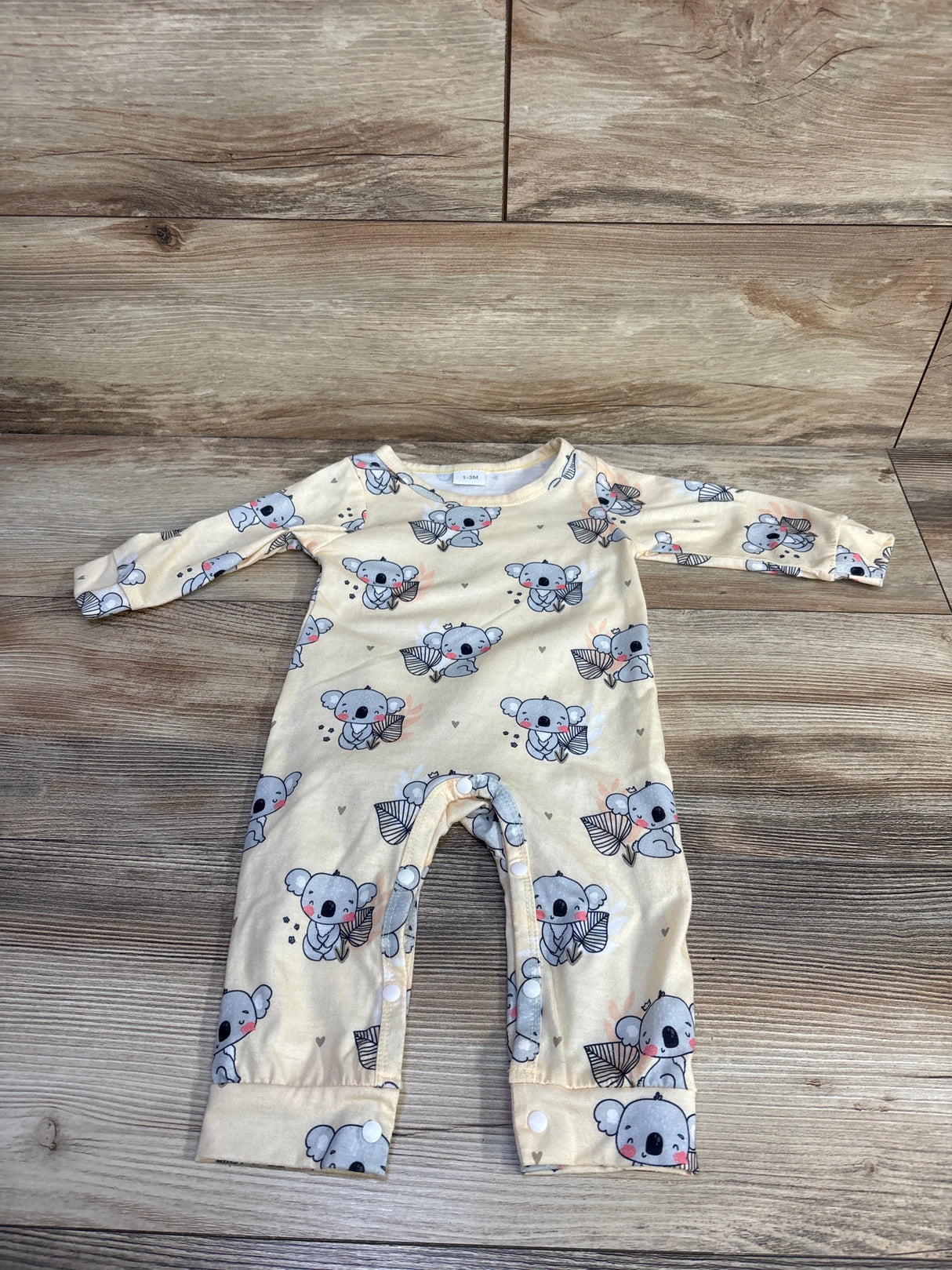 Flat lay of yellow newborn koala print coverall showing snap leg closures and fold-over cuffs on wood background