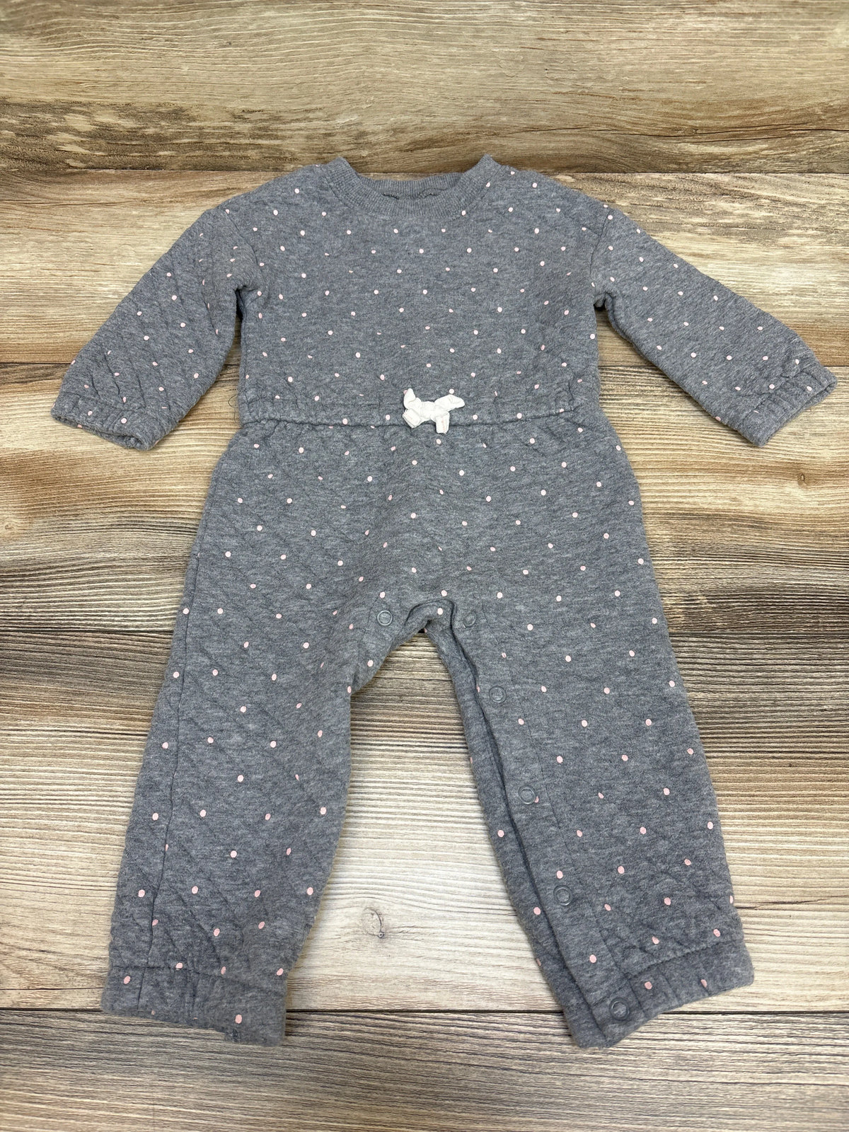 Front view of Carter’s gray quilted coverall with pink dots, white waist bow, and snap closures on wood background