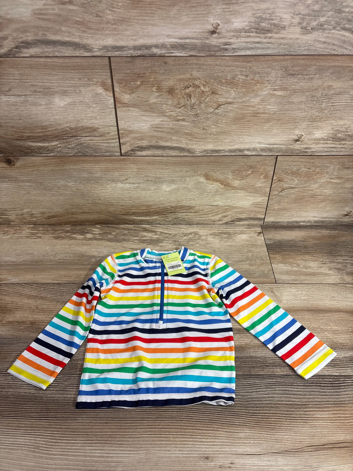 Flat lay of baby long-sleeve rash guard, rainbow stripes, front quarter-zip, size 12-18 months on wood floor