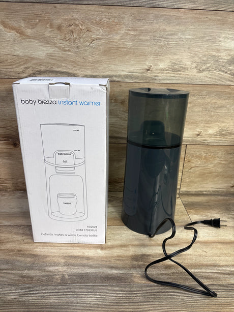 Front view of Baby Brezza Instant Bottle Warmer in black showing included box and power cord on wood background