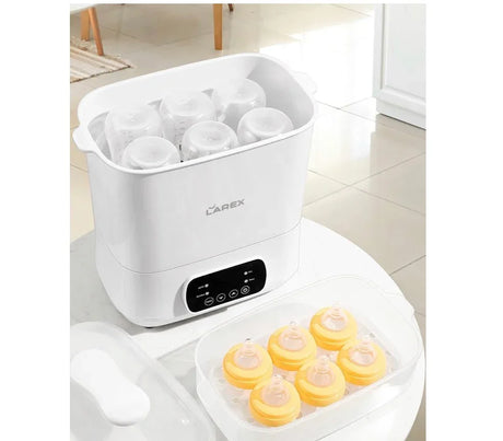Electric baby bottle sterilizer with clear lid and baby bottle nipples on a table.