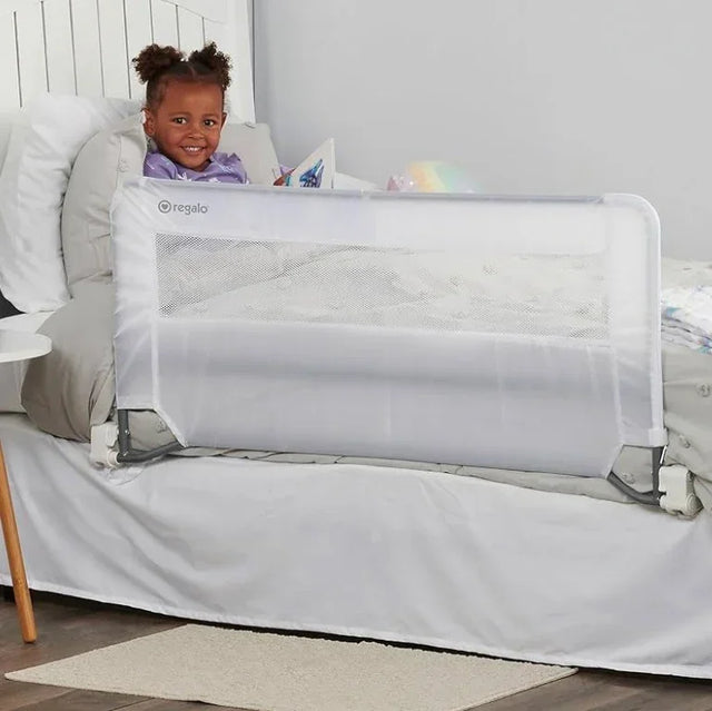 Side view of Regalo Guardian swing-down bedrail showing mesh panel and fold-down hinge on a white child's bed