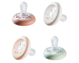 Four Tommee Tippee breast-like pacifiers (0 to 6 months) in pink, white and green showing rounded nipple and vented shields on white background