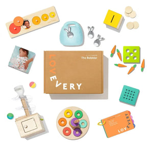 Top view of Lovevery Babbler play kit showing the box and assorted colorful wooden toys on white background