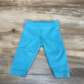 Flat lay of aqua baby leggings (0–3 months) showing elastic waistband and ankle hems on wood floor background