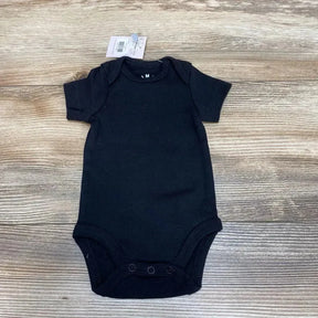 Top-down view of black organic cotton newborn bodysuit showcasing envelope shoulders and three-snap crotch on light wood background