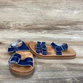 Angled overhead of navy Freshly Picked Rockaway sandals with double front straps, ankle buckle and tan stitched sole on wood