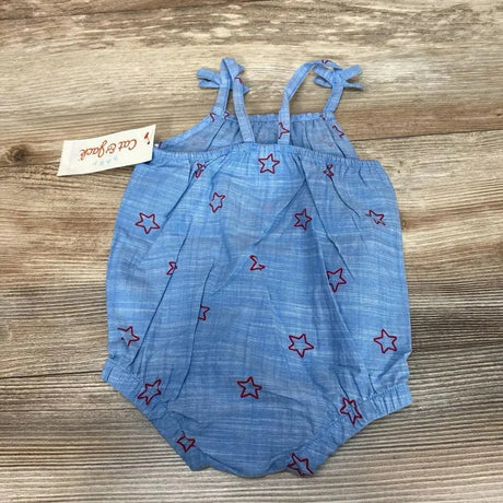 Flat lay of new Cat and Jack chambray romper showcasing blue tie strap bubble onesie with red star print and hangtag on wood plank floor