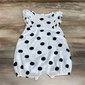 Flat lay of white polka-dot shortie romper with ruffle sleeves, snap crotch, and elastic leg openings on wooden floor