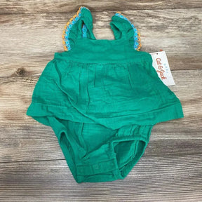 Top-down view of green muslin bodysuit dress showcasing ruffled lace-trim shoulder straps and snap crotch on wood background