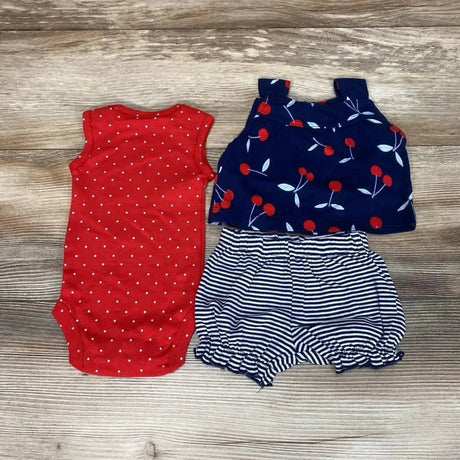 Flat lay of newborn 3-piece set: red polka-dot bodysuit, navy cherry-print top, navy-and-white striped bloomers on wood
