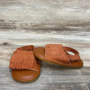 Three-quarter view of toddler Romirus fringe moccasins size 3C showing rust suede fringe and back strap on light wood surface