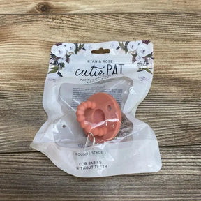 Top-down view of Ryan & Rose cutiePAT round pink pacifier with beaded teether in sealed packaging on wood background