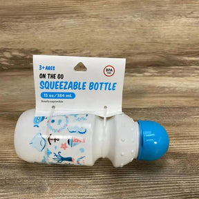 Side view of 13 oz squeezable baby bottle with blue cap, textured grip and nautical print on a wood tabletop