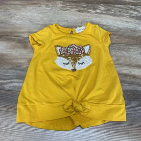 Flat lay of yellow short-sleeve toddler shirt showcasing sequin fox applique with floral crown and front knot on wood background