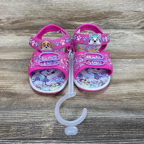 Front view of pink Paw Patrol ankle-strap sandals size 9C showing character patches and adjustable Velcro straps on wood