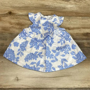 Flat lay of newborn white dress with blue floral print and matching bloomers showcasing flutter sleeves and gathered skirt on wood background