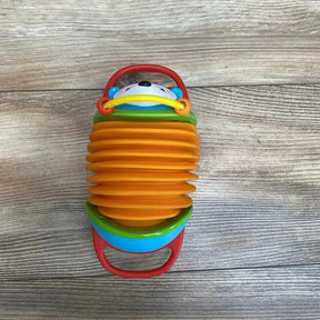 Top-down view of Skip Hop hedgehog accordion toy showcasing orange expandable bellows, red handles, and smiling hedgehog face on wood background